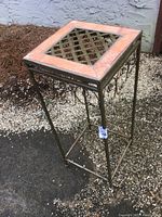 Side angled view of metal plant stand showing tile inlay and decorative scrollwork on legs
