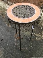 Front view of the metal plant stand showing tile border and intricate metal center on the top surface.