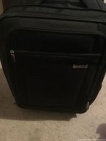 Front view of black Samsonite soft-sided luggage upright on floor, showing exterior front compartments and logo plaque.