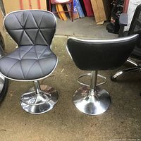 Two black leather bar stools facing opposite directions showing quilted seat and back detail and chrome bases with footrests.