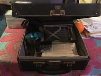 Showing vintage Polaroid camera and accessories inside an open black carrying case on fabric surface.