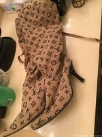 Side and front view of tan dress boots with dark brown Louis Vuitton monogram pattern, pointed shoes with mid-height black heels and fabric lace ties.