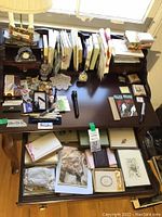 Overview of desk surface showing clock, inkwell, wax seal tools, pens, stationery piled on desk