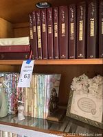 Top shelf showing a collection of dark maroon hardcover Bible books with gold lettering, floral journals and small decorative figurines.
