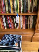 Two wooden shelves filled with various cookbooks mainly focusing on baking, desserts, pies, tarts, knitting, and cooking techniques.