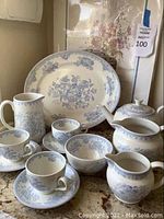 Entire china set displayed with platter, pitcher, teapot, sugar bowl, creamer, bowls, cups and saucers alongside framed floral print