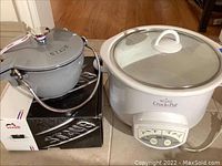 White Rival Crock-Pot Smart-Pot alongside Staub kettle on box
