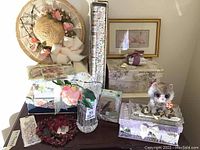 Wide view of the lot showing multiple decorative floral-themed boxes, a heavy textured glass vase, floral paper pack, framed art, and a decorative floral hat.