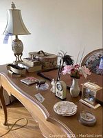 Desk surface with lamp, clocks, decorative boxes, vases, paperweight, and writing pad arranged