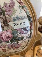 Close-up of the floral chair upholstery and its dimensions tag, showing floral tapestry fabric and a wooden rounded frame.