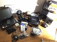 Lot showing Accurta DVD player, binoculars, various electronics, charger cables, and remote control on a wooden surface