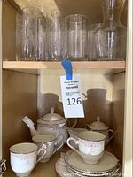 Photo of glass and stemware drinking glasses with etched floral designs, on top shelf of cabinet.