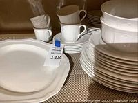 Photo showing stacked Mikasa white china plates, cups, saucers, and large platter, displaying quantity and design.