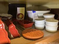 Shelf display showing two red ceramic bread loaf pans with scalloped edges beside white ceramic ramekins.
