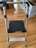 Full view of aluminum and plastic stepstool with one step and handle grips on each side.