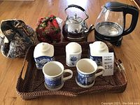 Overview of all items on the wicker tray including electric kettle, metal stovetop kettle, containers, mugs, and tea cozies.