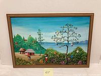 Front view of framed painting showing the full scene with huts, tree, people, ocean, and mountains.