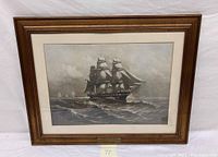 Framed naval print showing the ship on the water with waves and cloudy sky.