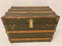 Full angled front view of antique steamer trunk showing wooden slats, metal hardware, and canvas covering