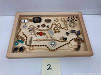 Overview of the full assortment of jewelry in a wooden tray including necklaces, earrings, brooches, and bracelets.