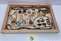 Full overview of costume jewelry lot displayed on a wooden tray showing necklaces, bracelets, earrings and pins including cameo pendant and various colorful designs.
