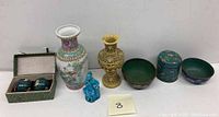 Full view of the lot including Famille Rose vase, carved cinnabar vase, turquoise folk figurine, pair of cloisonné meditation balls in box, and two small cloisonné lidded containers with bowls.