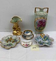 Group photo of six porcelain items including two vases, one teacup with saucer, and three trinket or nut dishes with floral and gold gilt decoration.