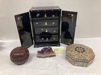 Photo showing the entire lot on a white surface: vintage black lacquer jewelry armoire with floral inlay, oval and octagonal lacquer boxes, and raw amethyst cluster.