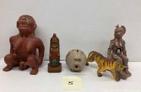 Five total pottery figures shown from left to right: large seated male figure, small ethnic totem, round piggy bank, painted tiger figurine, and large female figurine with hole in stomach