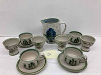 Full set displayed including pitcher, four dessert cups, two handled cups and saucers on white background.