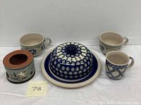 Set of vintage Stangl and Polish Pottery including covered butter dish with plate, three floral mugs, and a ceramic candle holder.