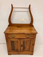 Front view of vintage maple wash stand with towel bar, drawer, and cabinet with brass handles