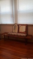 Wooden slatted bench with cushion placed in front of window on hardwood floor