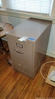 Side angle view of beige metal 2-drawer file cabinet with visible signs of wear and label holder on top drawer.