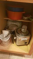 Shelf showing Cuisinart electric grinder, orange and blue pots, and small kitchen gadgets