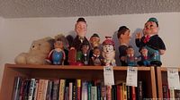 Shelf with multiple collectible items including Laurel and Hardy figures, stein, plastic banks, and small figurines alongside two stuffed animals in the background.