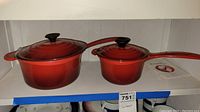 Two red enameled cast iron pots with lids side by side on shelf