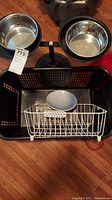 Photo showing 2-space black pet feeder stand with two stainless steel bowls, black plastic basket, white metal dish drainer, and gray plate