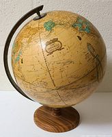 Full view of the Cram's Imperial world globe mounted on a wooden circular base with a metal semi-meridian arm for rotation. The globe surface shows age with an antique color tone and detailed geographic labeling.