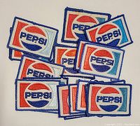 Top view of 20 vintage rectangular embroidered Pepsi patches arranged overlapping on a white surface.