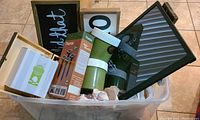 Photo showing multiple framed wall decor signs, garden solar stakes box, and other household decorative items in a large plastic bin.