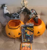 Two large orange blow mold jack o lanterns with Halloween figures and props on a couch with vinyl tablecloth and lawn bags in front.