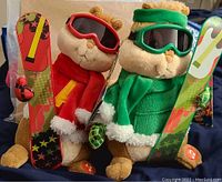 Two plush Alvin and the Chipmunks toys in festive ski gear holding snowboards