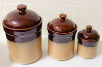 Three Sango Nova Brown ceramic canisters of varying sizes with lids, showing color gradient from brown to beige.