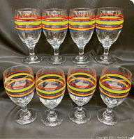 Eight Libbey Fiesta Mambo striped glasses, clear with red, yellow, blue bands, arranged in two rows.