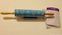 Ceramic rolling pin with blue floral pattern resting on matching ceramic stand with instruction sheet visible.