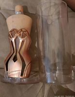 Photo of Jean Paul Gaultier Classique body lotion bottle shaped like female torso with metallic rose gold corset and clear plastic case.