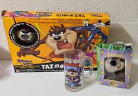 Photo shows all three lot items including the Tazmania game box in back, the Taz glass mug in front center, and Six Flags branded Taz plush on the right side.