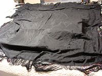 Full view of the large black shawl showcasing the overall shape, size, and texture with fringe along the edges.