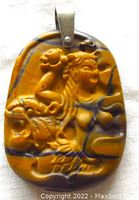 Front view of the tiger eye pendant showing intricate carvings of a lady, fish, and tiger.